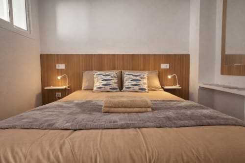Modern bedroom in La Aldea vacation apartment with wooden headboard, white pillows, beige bedding, and twin reading lamps