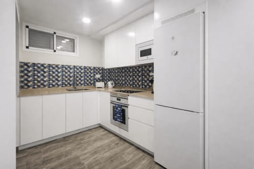 Modern white kitchen with geometric blue tile backsplash, wood countertops, stainless steel appliances and refrigerator in La
