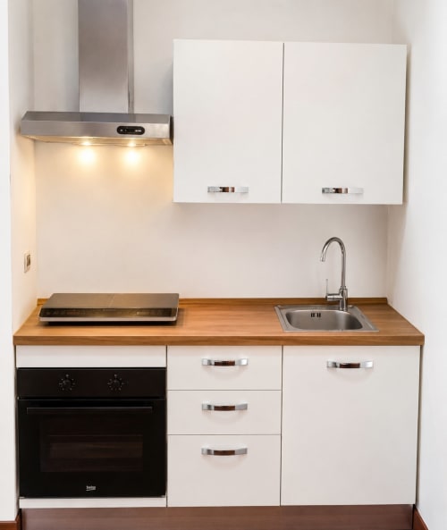Cucina moderna e compatta dell'appartamento Myob Roma con lavello in acciaio inox, forno nero, piano di lavoro in legno e mobili bianchi