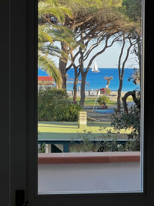 Sea view from Casa Rossa villa at Casa Pineta, Marina di Campo, with palm trees, sailboat, and Mediterranean coastline