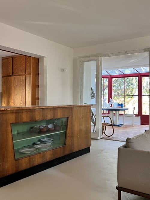 Modern living room at Casa Pineta villa with wooden display cabinet, green shelving, and view to red-framed conservatory