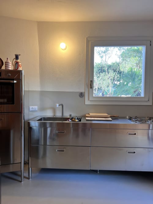 Modern stainless steel kitchen with sink, window overlooking tropical trees at Casa Pineta villa, Marina di Campo