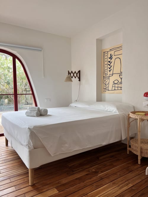 Bright modern bedroom at Casa Pineta with white bed, wooden floor, sea view through arched window, and minimalist décor in