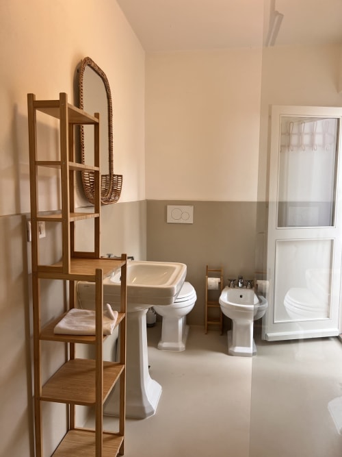 Bathroom display at Casa Pineta villa in Marina di Campo featuring white pedestal sinks, toilet, and wooden shelving unit