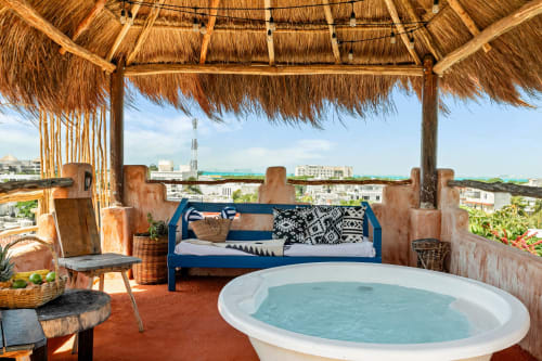 Rooftop terrace with soaking tub, blue couch, and thatched palapa overlooking Isla Mujeres with turquoise ocean view