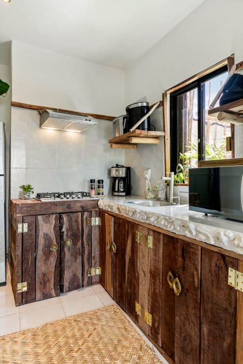 Modern kitchen with wooden cabinetry, gas stove, and sink in Isla Mujeres apartment with garden views through open doors