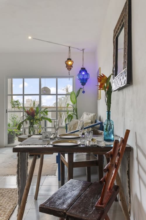 Dining area with garden view at Isla Mujeres apartment, wooden table, blue pendant lights, potted flowers, and terrace access