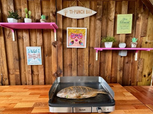 Bar Ti-Punch avec poisson grillé sur plancha Tefal, décoration murale en bois, étagères roses et plantes tropicales chez Kay Lakansiel