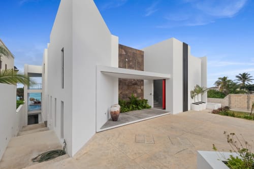 Modern white villa with sea view entrance in Isla Mujeres featuring red door and stone accents