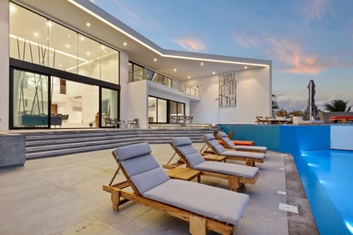 Modern beachfront villa with wooden lounge chairs, infinity pool, and glass-fronted house at sunset, Isla Mujeres