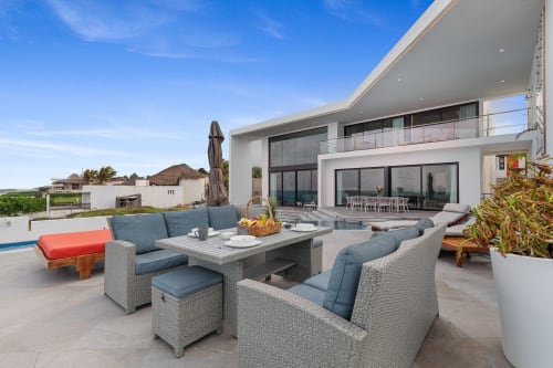 Luxury villa patio with woven lounge furniture, pool view, and modern white building in Isla Mujeres