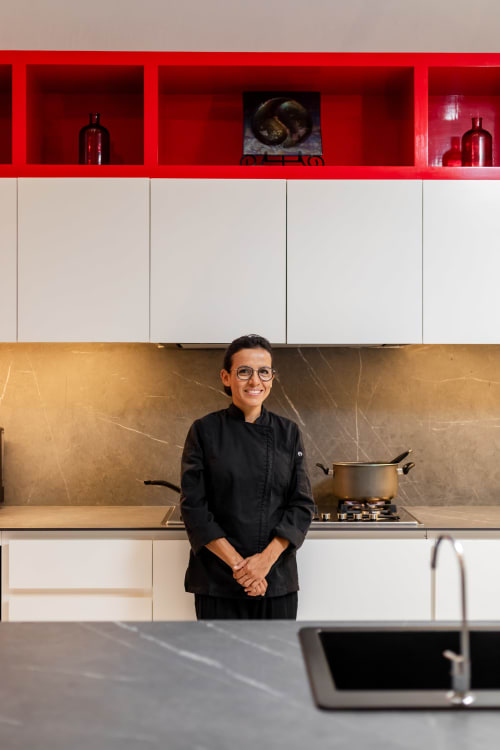 Chef smiling in modern kitchen of Isla Mujeres villa with red shelving, gold backsplash, and cooktop