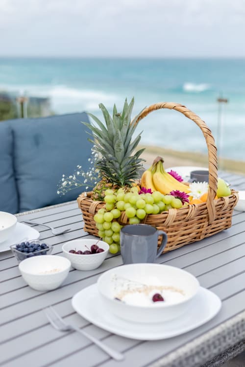Beachfront villa breakfast setup with tropical fruit basket, white place settings, and ocean view at Isla Mujeres