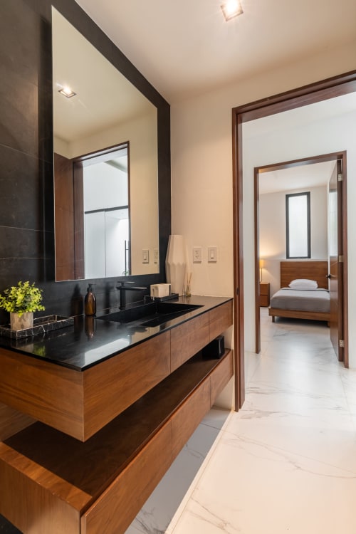 Modern bathroom at Villa E11even, Isla Mujeres with wood vanity, black countertop, and bedroom view