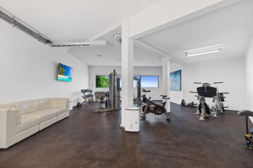 Modern home gym at Isla Mujeres villa with exercise bikes, equipment, cream sofa, and sea view artwork