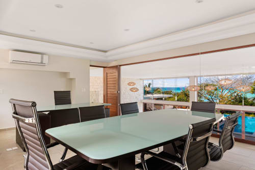 Modern villa dining room with ocean view, glass table, black chairs, and Caribbean Sea visible through floor-to-ceiling