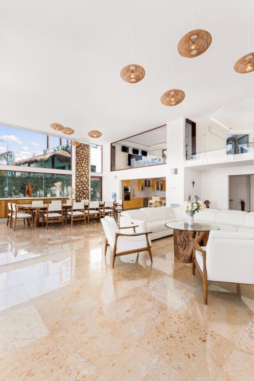 Spacious villa living area with travertine floors, white seating, wooden accents, woven ceiling fixtures, and sea views at