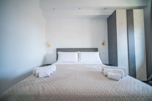 Camera da letto dell'appartamento Argiro Deluxe presso l'hotel Newhouse di Bari con testata grigia, biancheria bianca e applique dorate
