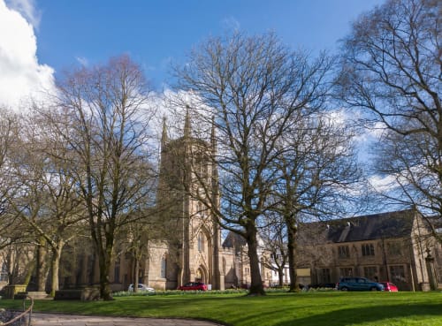 Historic stone church with tall spire surrounded by bare trees and manicured lawns at The Courtyard by JS Apartments, GB