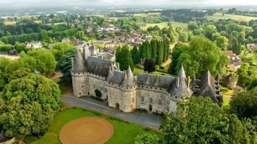 Vue aérienne du château historique de Châlus avec ses tours, entouré de pelouses verdoyantes, d'arbres et de bâtiments villageois en France rurale