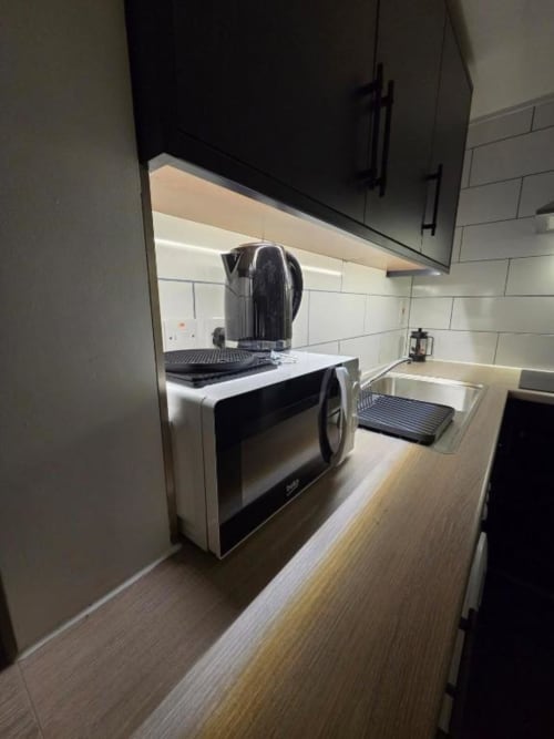 Modern kitchen at The Snug by JS Apartments in Blackburn with black cabinets, stainless steel microwave, and white subway