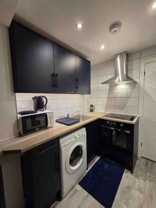 Modern kitchen at The Snug by JS Apartments, Blackburn with black cabinetry, white subway tiles, and stainless steel