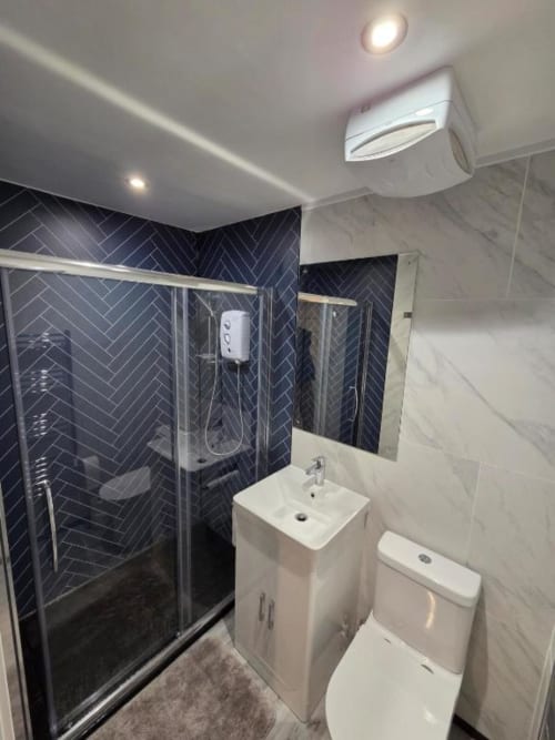 Modern bathroom at The Snug by JS Apartments in Blackburn with black herringbone tiles, white sink, toilet, and glass shower