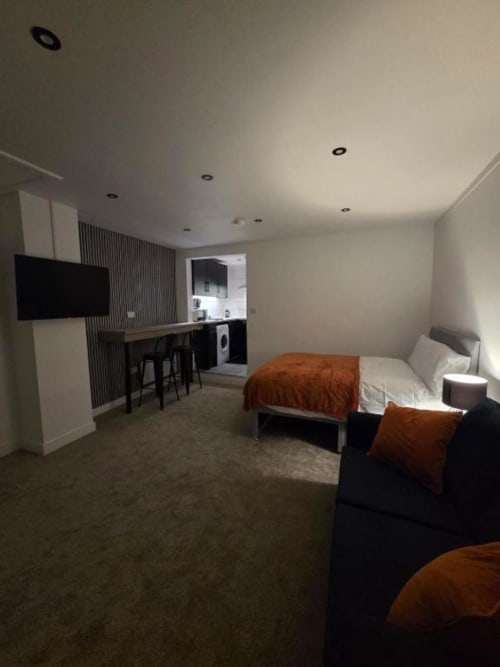 Modern studio apartment at The Courtyard by JS Apartments in Blackburn featuring bed with orange throw, kitchenette, TV, and
