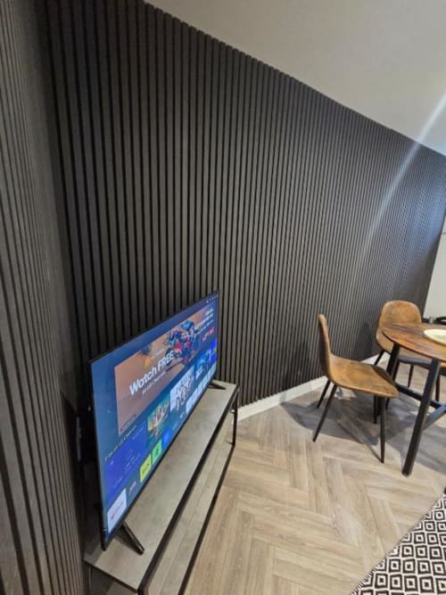 Modern apartment lounge at Courtyard by JS Apartments Blackburn with TV, wooden chairs, and contemporary textured wall