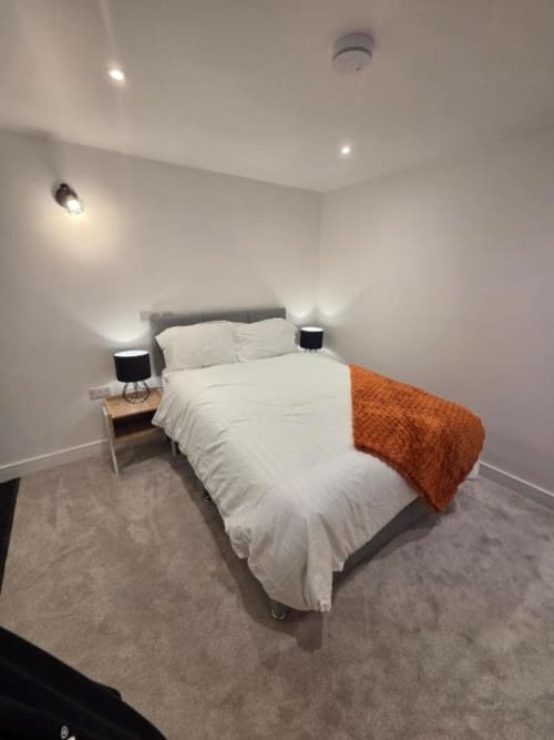 Modern bedroom at The Courtyard by JS Apartments in Blackburn with white bedding, orange throw, bedside lamps, and recessed