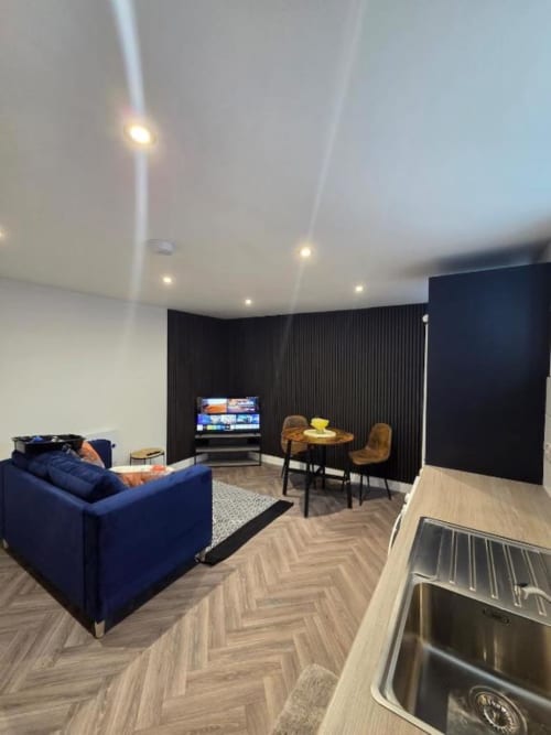 Modern studio apartment at The Courtyard by JS Apartments in Blackburn featuring blue sofa, dining area, TV, and herringbone