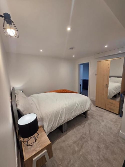 Modern bedroom at The Courtyard by JS Apartments in Blackburn with white bedding, wooden wardrobe, and ambient lighting