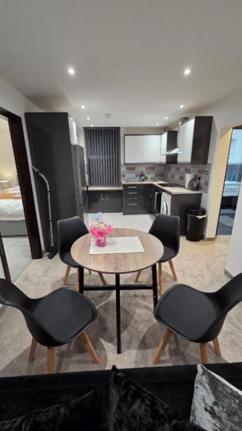 Family Flat dining area with round table and black chairs, modern kitchen with dark cabinets at The Courtyard by JS