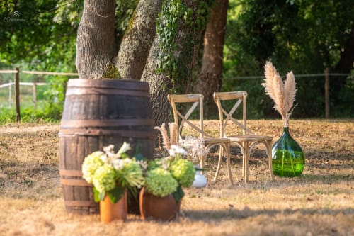 Rustic outdoor event setup at Domaine De Bafave with wooden chairs, barrel, and pampas grass decorations under shaded trees