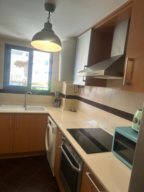 Cocina moderna en apartamento Sant Jordi con electrodomésticos de acero inoxidable, encimeras color crema, gabinetes de madera y lámpara colgante