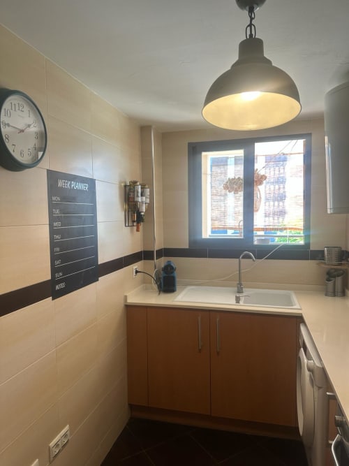 Fregadero de cocina moderno con grifo de acero inoxidable, armarios de madera, lámpara colgante y organizador semanal en la pared en Sant Jordi