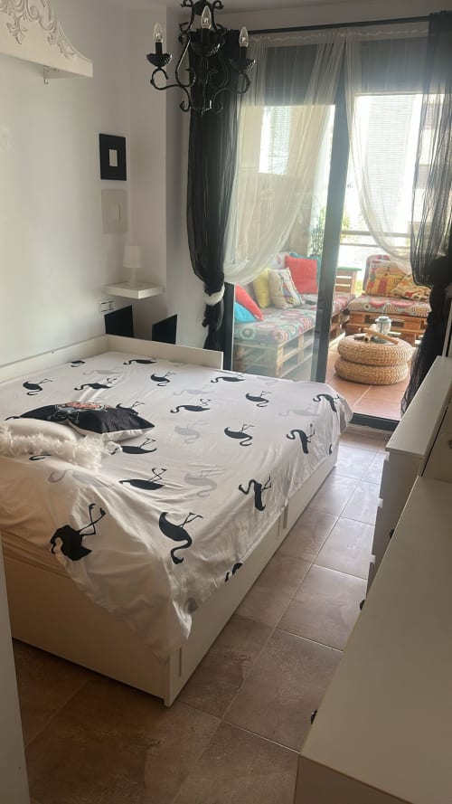 Dormitorio acogedor en Sant Jordi con cama blanca, lámpara de araña de hierro forjado negro y acceso a terraza amueblada