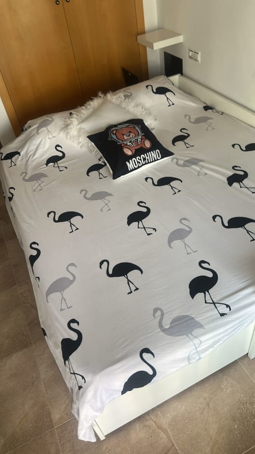 Ropa de cama blanca con patrón de flamencos en negro y gris en el apartamento Sant Jordi, con armario de madera y almohada Moschino.