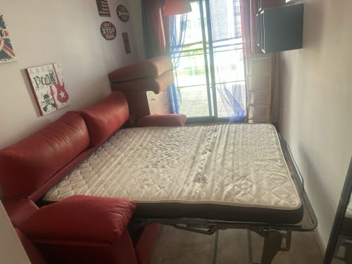 Dormitorio acogedor con sofá de cuero rojo, colchón y puerta de cristal que abre a balcón con vistas a la montaña en Sant Jordi