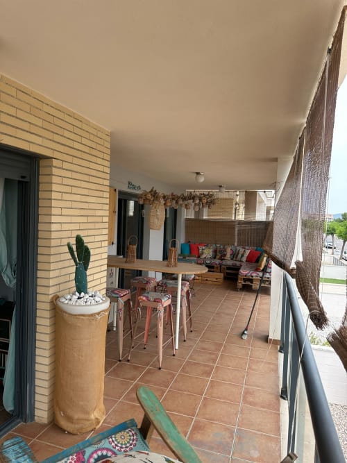 Amplia terraza cubierta con suelo de baldosas, barra de bar, cojines coloridos, cactus en maceta y vistas a las montañas en Sant Jordi