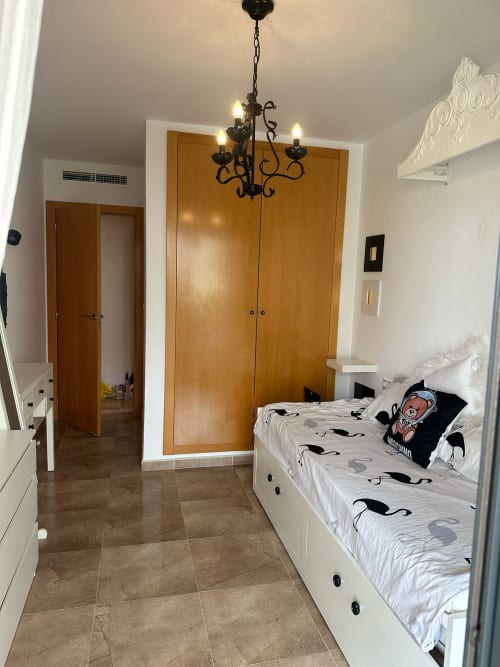 Dormitorio espacioso con cama blanca, armario de madera, araña y suelo de baldosas en el apartamento Sant Jordi