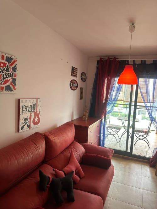 Salón moderno con sofá rojo, lámpara colgante naranja y vistas al balcón del apartamento Sant Jordi