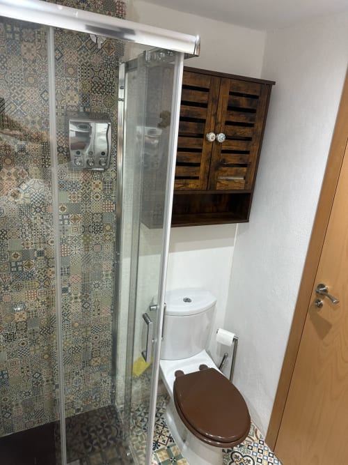Baño moderno en apartamento Sant Jordi con ducha de azulejos decorativos, inodoro blanco, tocador de madera y toallero radiante