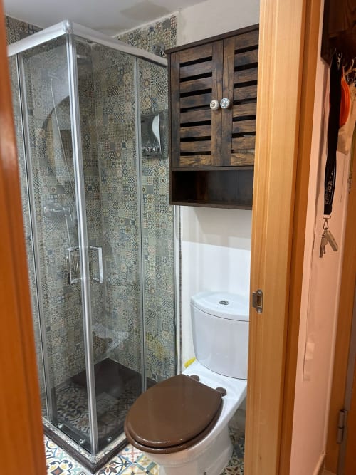 Baño moderno con ducha de azulejos mosaico, tapa de inodoro marrón y mueble de almacenamiento de madera en el apartamento Sant Jordi