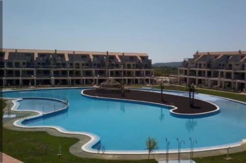 Piscina azul con formas curvas y paisajismo en el complejo Sant Jordi, rodeada de edificios en terrazas con vistas a la montaña