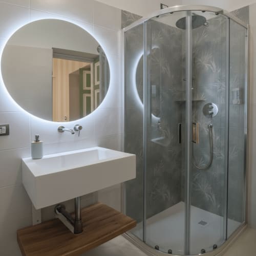 Bagno moderno in Camera Neve presso Il 900 B&B, Avezzano, con specchio circolare illuminato a LED e doccia in vetro