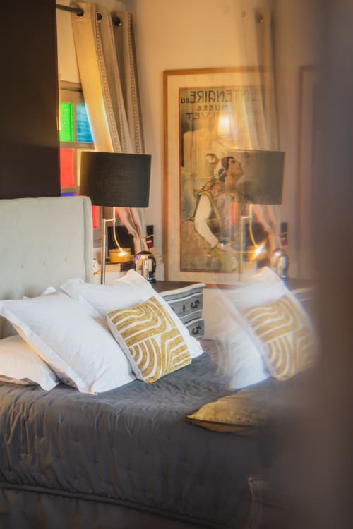 Chambre moderne aux Jardins de Baracane avec oreillers blancs, coussins dorés et œuvres encadrées à Avignon