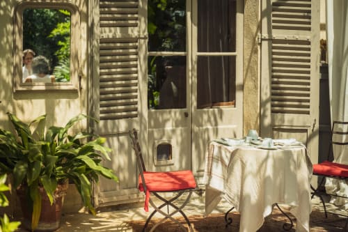 Cour ensoleillée aux Jardins de Baracane avec chaises rouges, table, plantes en pot et volets à Avignon