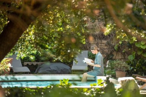 Femme lisant au bord de la piscine aux Jardins de Baracane, une oasis paisible à Avignon entourée de verdure