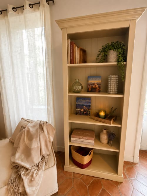 Bibliothèque en bois crème avec livres décorés, plantes et bougies dans une chambre d'hôtes de style français